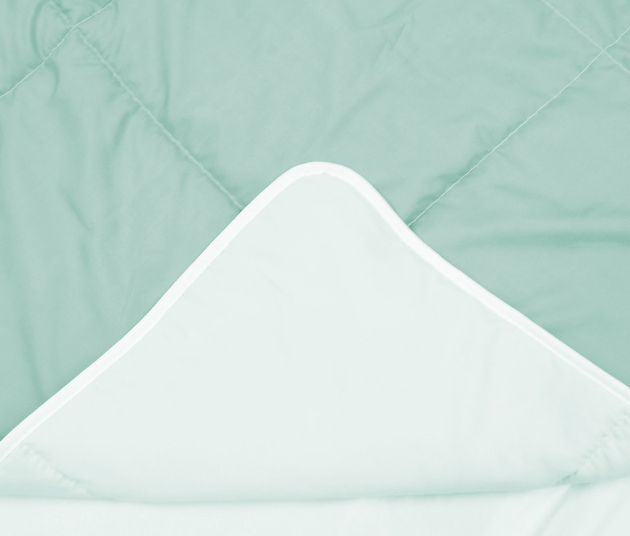 Eine mintgrüne Paradies Sommerdecke »Easy-Care« mit gestepptem Muster, deren Ecke umgeschlagen ist und die hellere Unterseite mit weißem Rand zeigt.