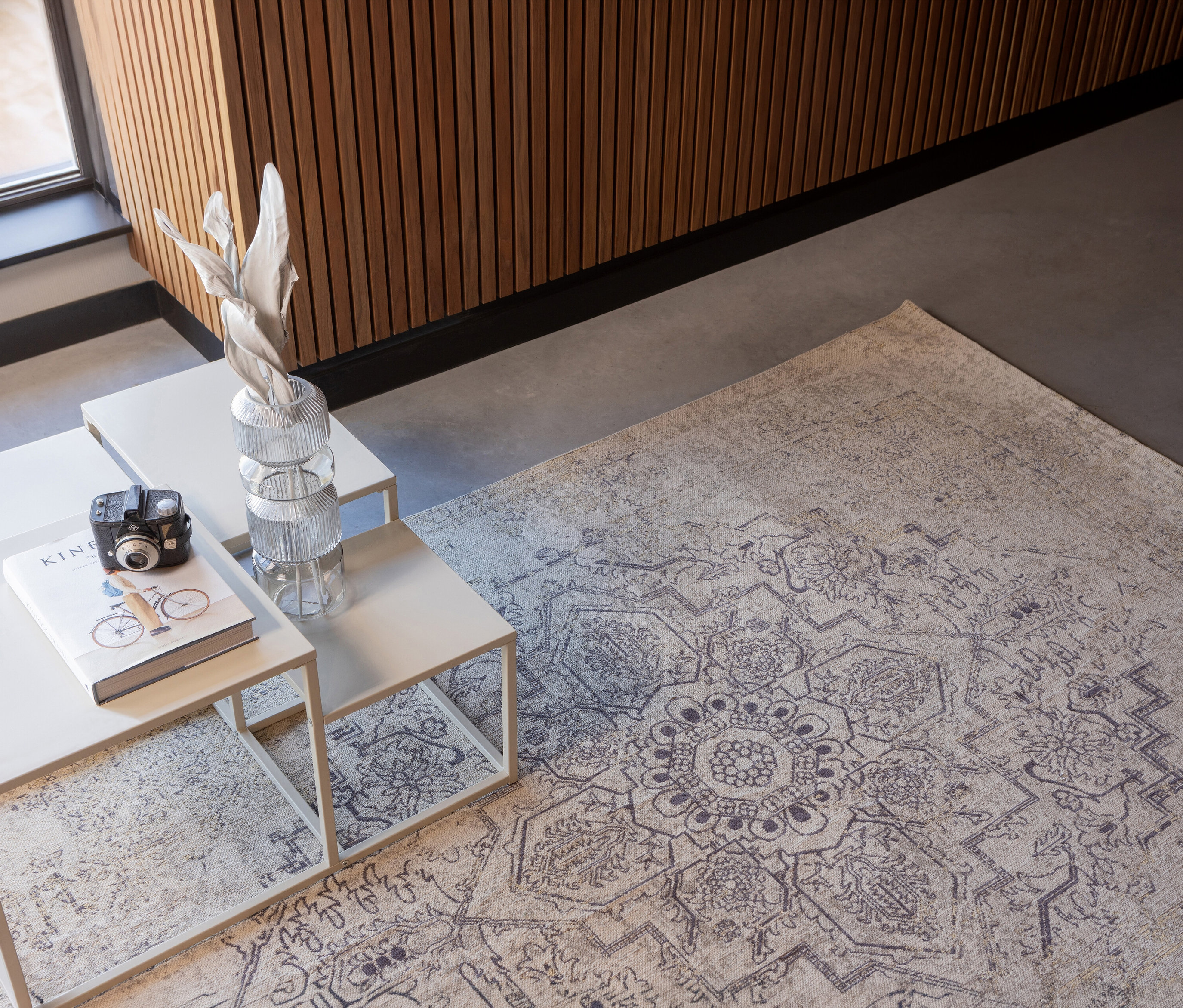 Auf grauem Boden liegt der mehrfarbige Woood Teppich »Eric« (170 x 240 cm). Darauf stehen drei Tische mit Deko.