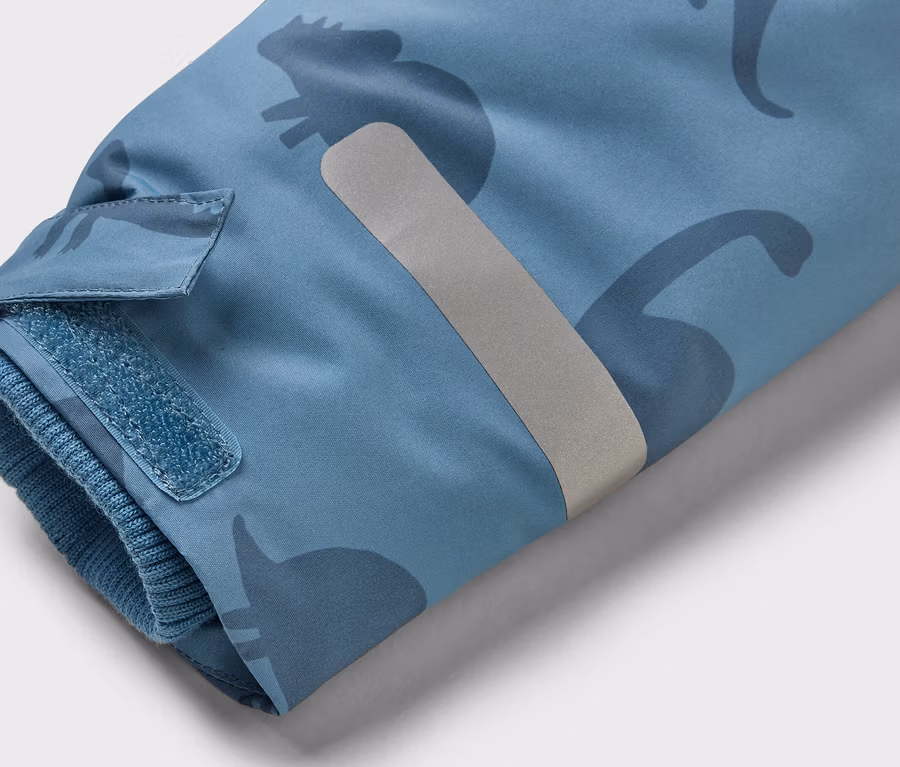 Ärmel einer hellblauen Jacke mit dunkleren Dinosaurier-Silhouetten, Klettverschluss und reflektierendem Streifen.