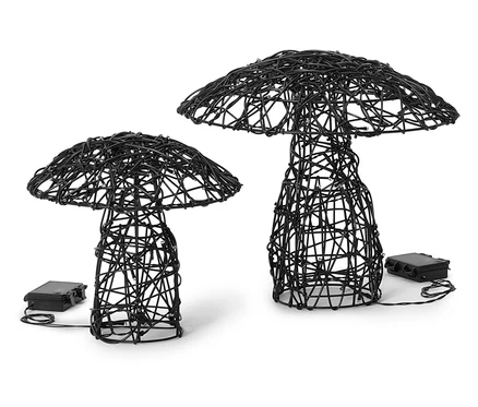 Zwei pilzförmige, schwarze Drahtlampen unterschiedlicher Größe stehen auf einem weißen Untergrund. Die Lampen sind beleuchtet.
