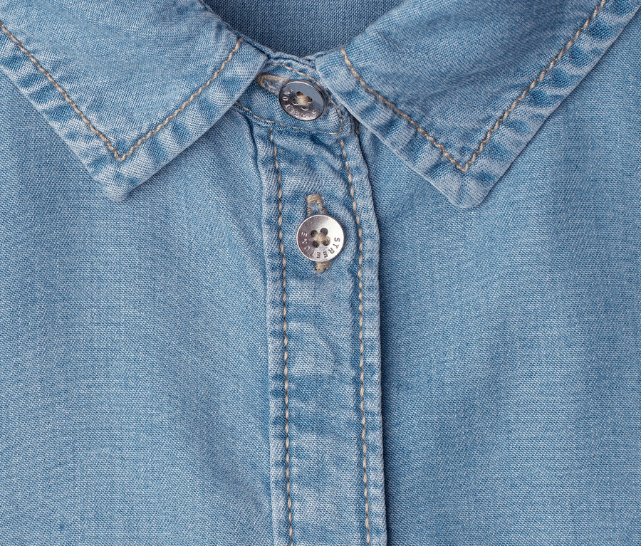Nahaufnahme eines hellblauen Jeanshemds mit Kragen und zwei silbernen Knöpfen.