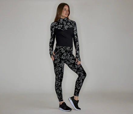 Frau in floral gemustertem, langärmligem Oberteil und Leggings, dazu schwarze Turnschuhe.