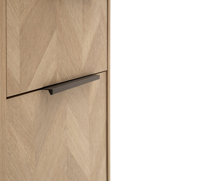 Nahaufnahme eines Holzschranks mit Fischgrätenmuster und einem dunklen, horizontalen Griff an einer Schublade.