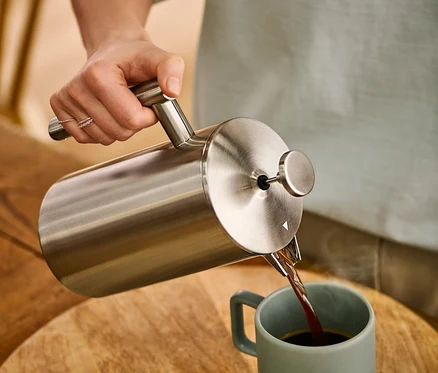 Frau gießt Kaffee aus einer doppelwandigen Siebstempelkanne aus Edelstahl mit 900 ml in eine Tasse.