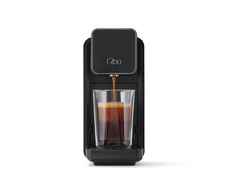 Schwarze »Qbo ONE« Kapselmaschine, Soft Black, die Kaffee in ein klares Glas füllt.