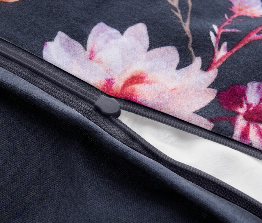 Nahaufnahme eines dunkelgrauen Stoffes mit Blumenmuster aus rosa und lila Blüten, teilweise geöffnet mit einem weißen Futter. Ein grauer Reißverschlusszipper ist sichtbar.