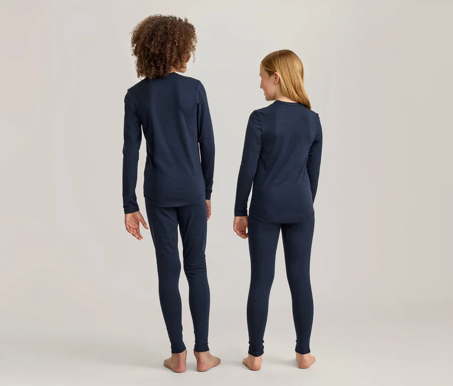 Zwei Kinder, ein Junge und ein Mädchen, stehen mit dem Rücken zur Kamera und tragen dunkelblaue Langarmshirts und Leggings. Der Junge hat lockiges Haar, das Mädchen glattes blondes Haar.