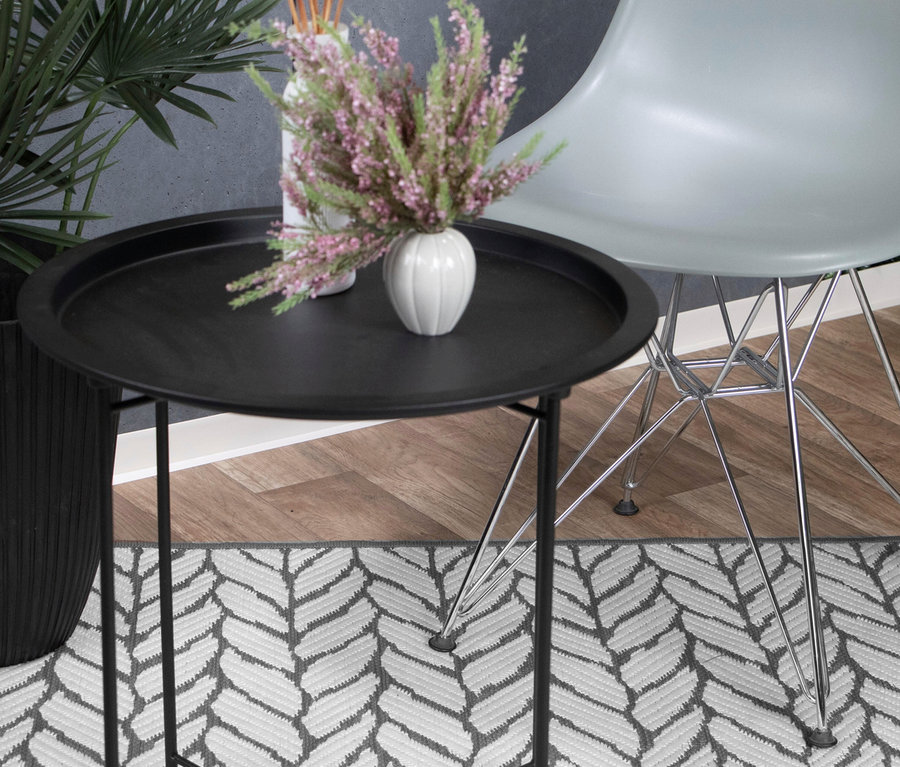 Schwarzer runder Beistelltisch mit weißer Vase voller rosa Blumen und Diffusorstäbchen auf grauem Outdoor-Wendeteppich »Knitted Joy«. Heller Stuhl und Pflanze im Hintergrund.