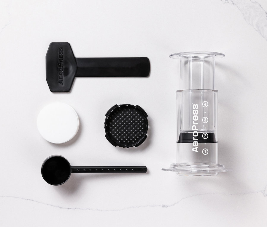 Einzelteile des transparenten AeroPress Coffee Maker »Clear« liegen auf einer weißen Oberfläche.