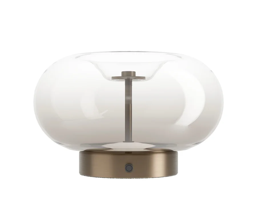 Eine moderne Tischlampe mit einem klaren, leicht rauchigen, pilzförmigen Glasschirm und einem gebürsteten Messingsockel. Eine dunkle Metallstange ragt von der Basis in die Mitte des Glases. Ein kleiner, runder Knopf ist an der Vorderseite des Sockels sichtbar.
