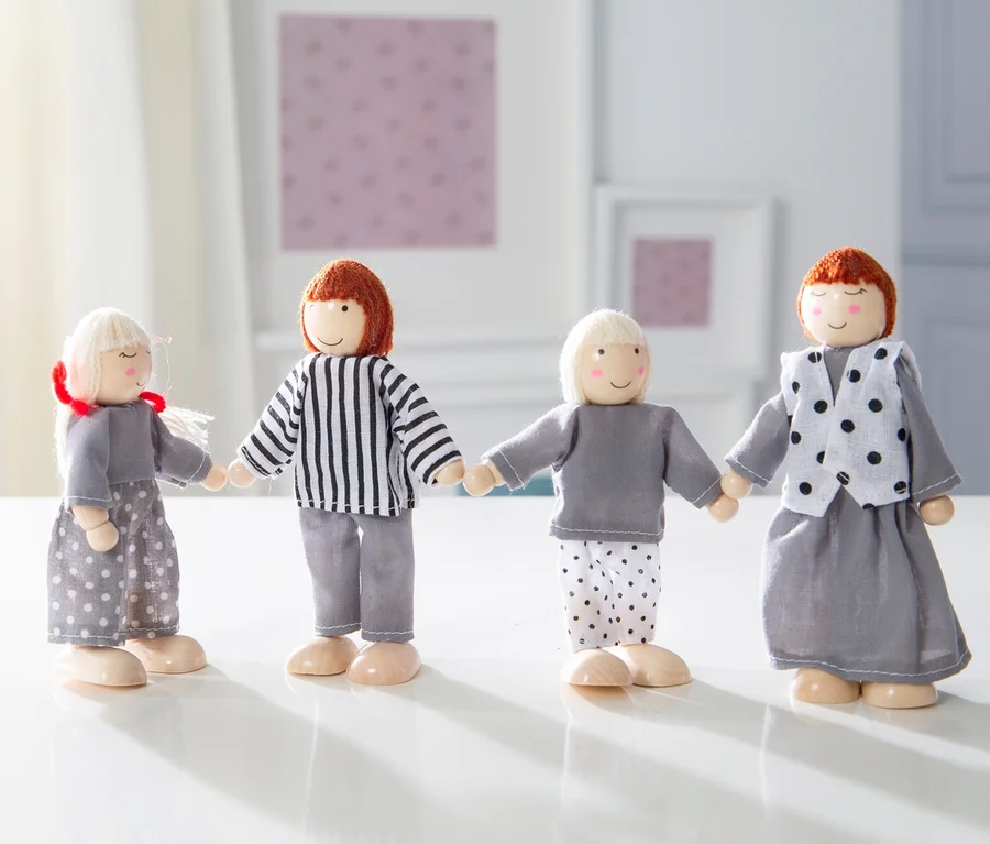 Vier Holzfiguren aus dem roba Puppenhaus inkl. Zubehör stehen nebeneinander und halten sich an den Händen auf einem weißen Tisch.