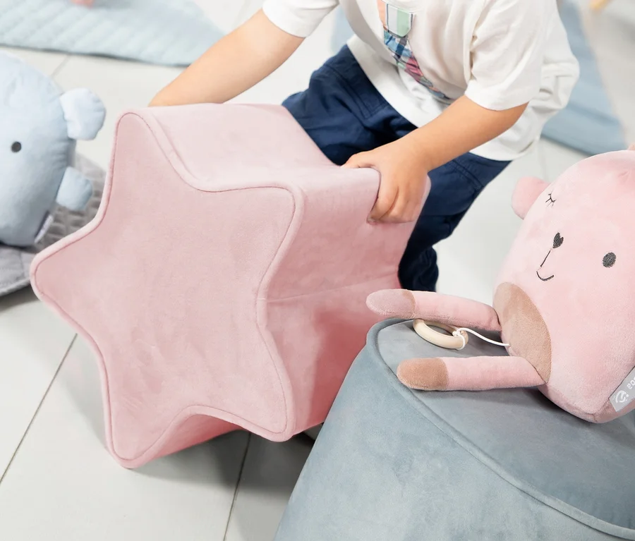 Junge hebt rosa roba Kinderhocker in Sternform »Lil Sofa« hoch.