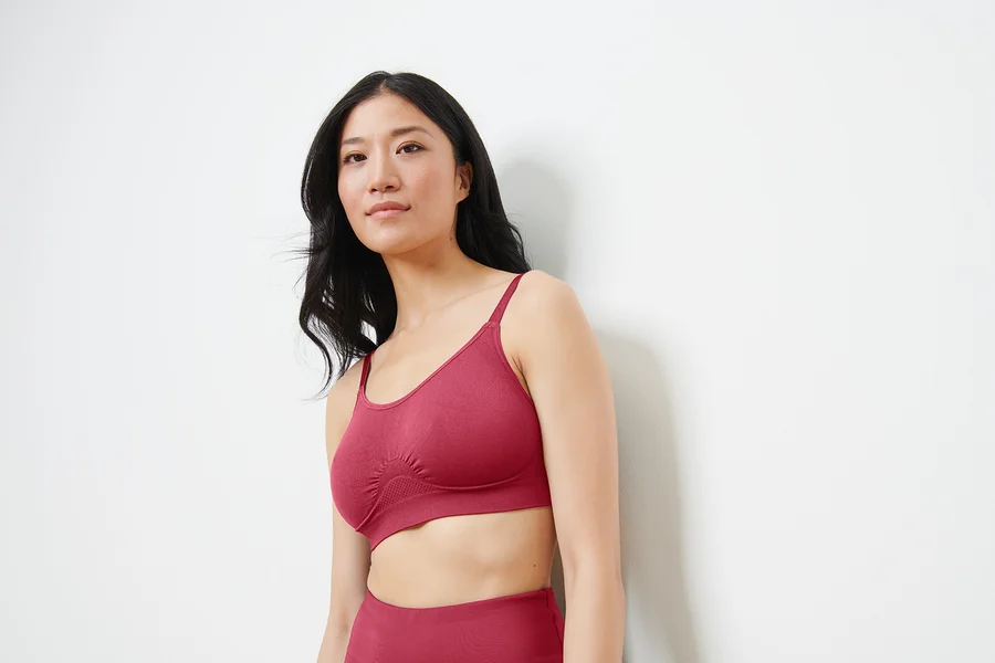 Asiatische Frau trägt einen nahtlosen Sport-BH in Beere-Farbe und schaut nach rechts.