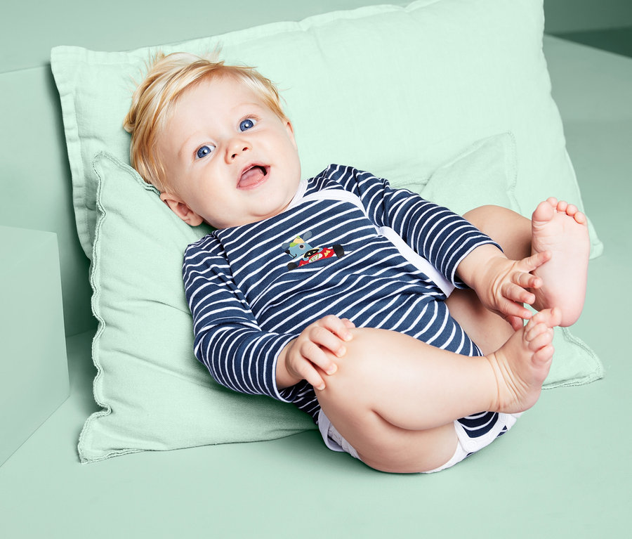 Lächelndes Baby liegt auf dem Rücken und trägt einen blau-gestreiften 3 Langarm-Body.