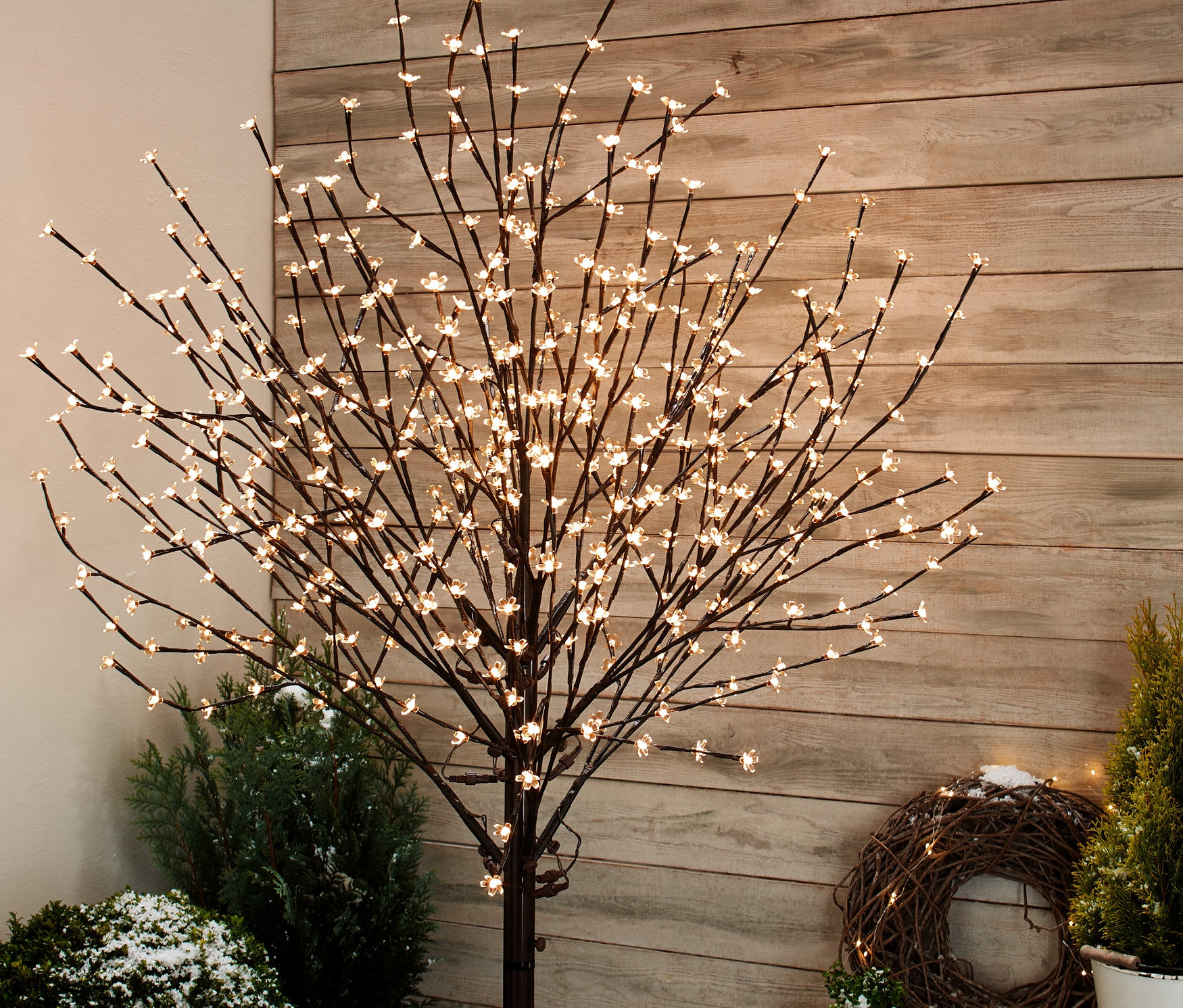 Ein LED-Baum mit Blüten steht draußen zwischen Pflanzen.