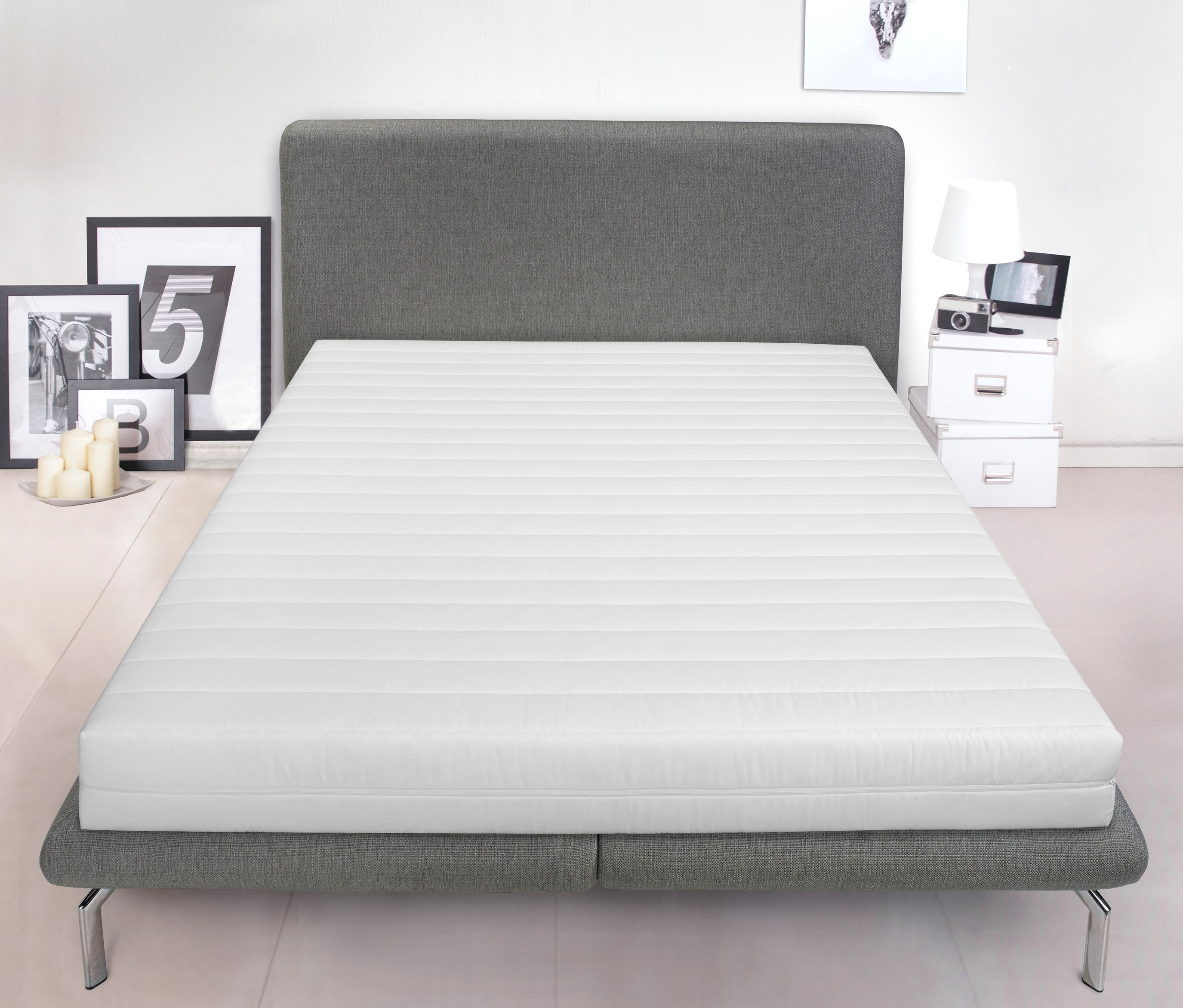 Eine weiße Badenia-Kaltschaummatratze »Duo« liegt auf einem grauen Bett. Hinter dem Bett stehen Dekoartikel.
