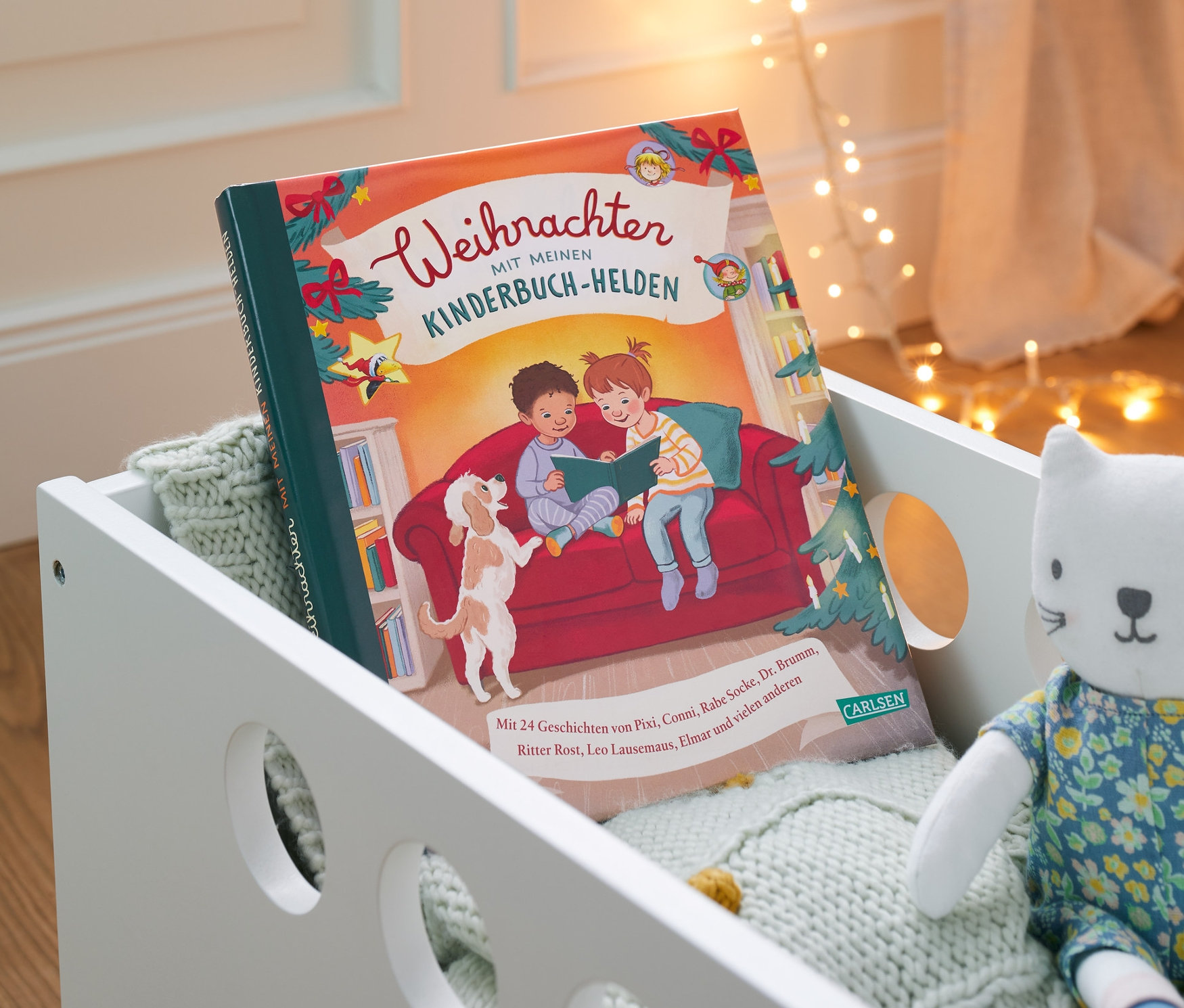 Buch "Weihnachten mit meinen Kinderbuch-Helden" liegt in einem weißen Spielzeugwagen mit einer Katzenpuppe.