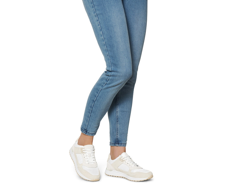 Beine einer Frau in Jeans und Veloursleder-Sneakern.