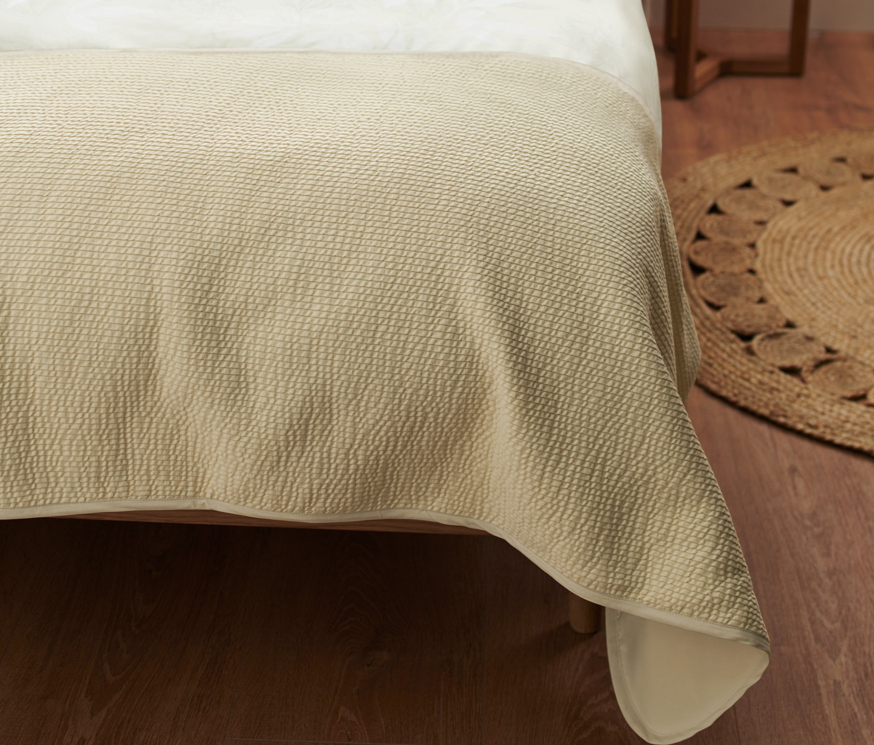 Schlafzimmer mit beiger Bettwäsche, weißen und grünen Kissen und einem hölzernen Nachttisch mit Lampe. Bettläufer.