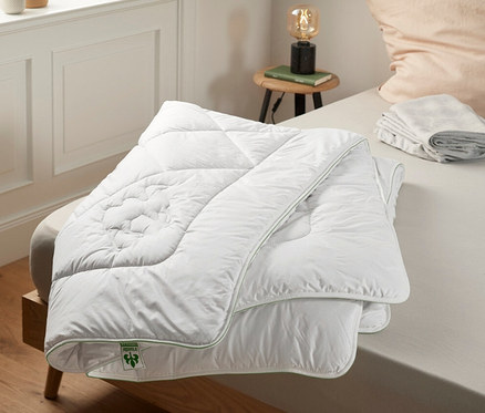 Auf einem Bett liegt eine weiße irisette® greenline Duo-Kamelhaarbett.