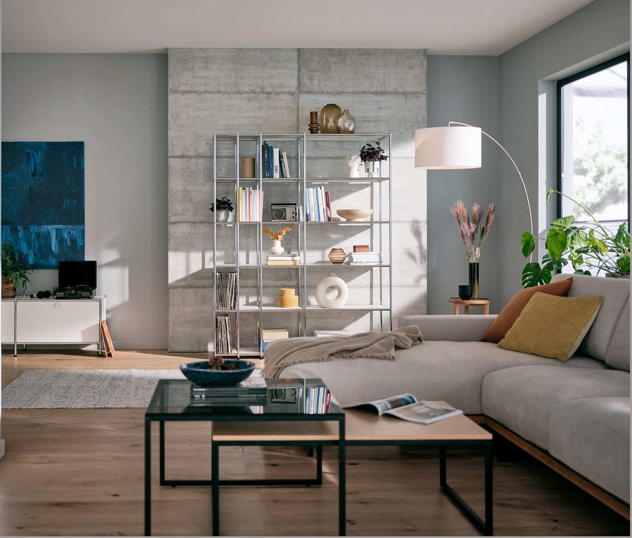 Wohnzimmer mit einem weißen, offenen Regal Metall »CN3«, einer Stehleuchte mit Textilschirm und einem zweiteiligen Couchtisch-Set.