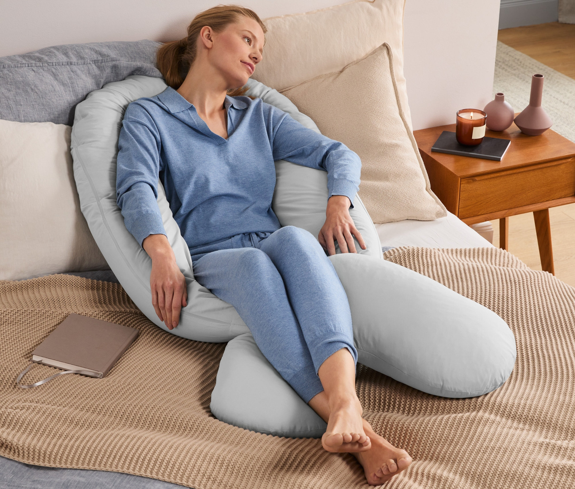 Frau sitzt im Bett, umgeben von einem XXL-Multifunktionskissen.