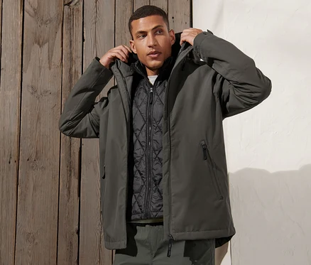 Mann justiert Kapuze der grüngrauen 3-in-1-Outdoorjacke mit Weste.