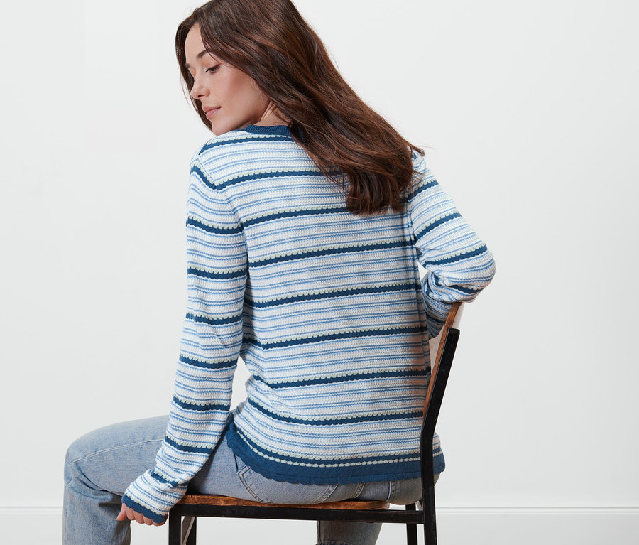 Frau sitzt auf einem Stuhl und trägt einen Feinstrickpullover mit blauen Streifen.