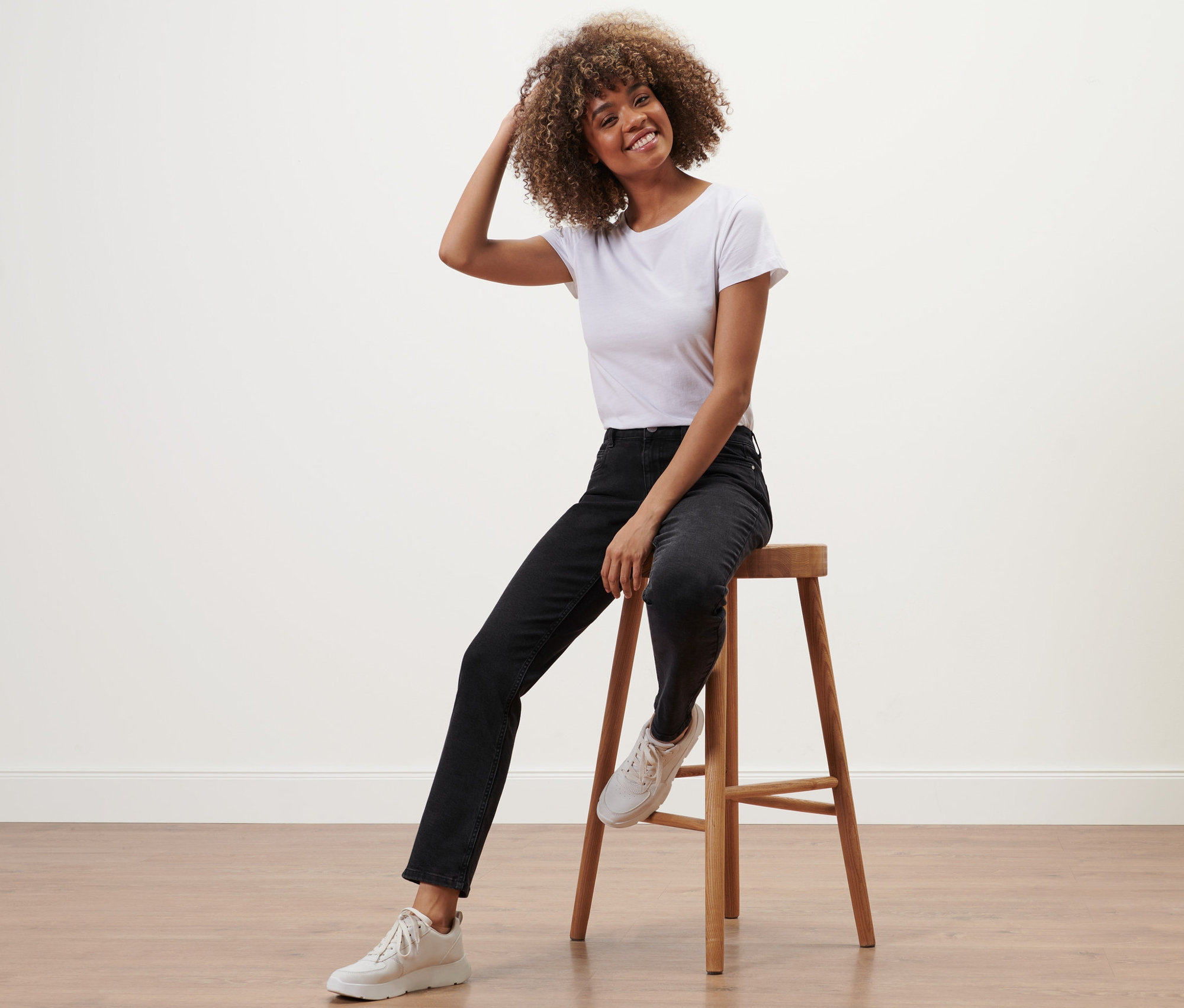 Frau sitzt auf einem Hocker und trägt eine schwarze Straight-Denim »Fit Juna«.