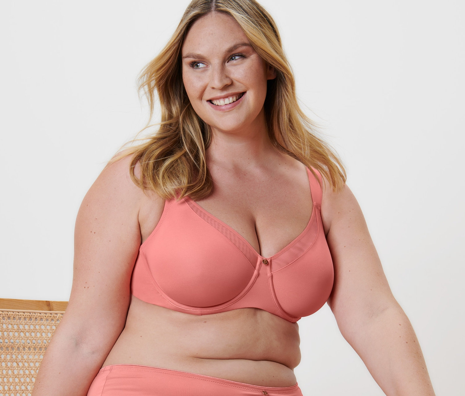 Frau sitzt auf einem Stuhl und trägt einen apricotfarbenen Minimizer-BH.