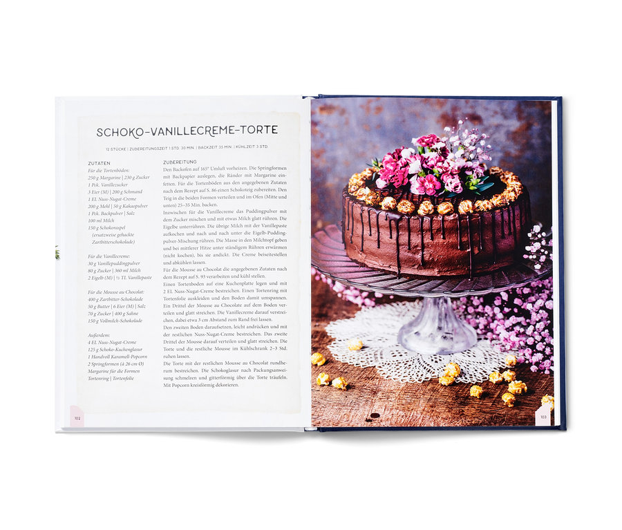 Aufgeschlagenes Kochbuch zeigt Schoko-Vanillecreme-Torte, dekoriert mit Blumen und Popcorn.