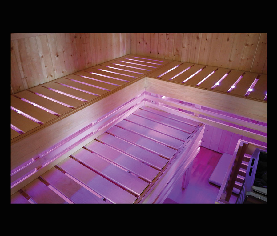 Innenansicht des Karibu Hybrid-Saunahauses »Alice 3« mit Holzbänken und violetter Beleuchtung.