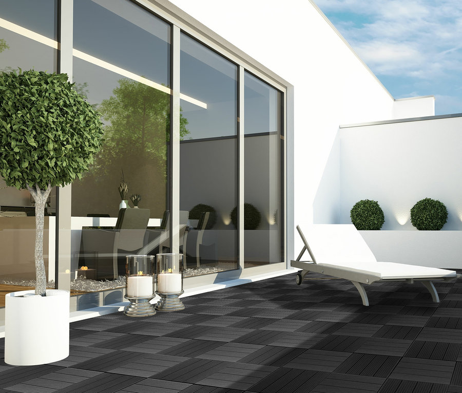 Terrasse mit dunkelgrauen 30 x 30 cm WPC Terrassenfliesen, Liegestuhl und Zierbüschen.