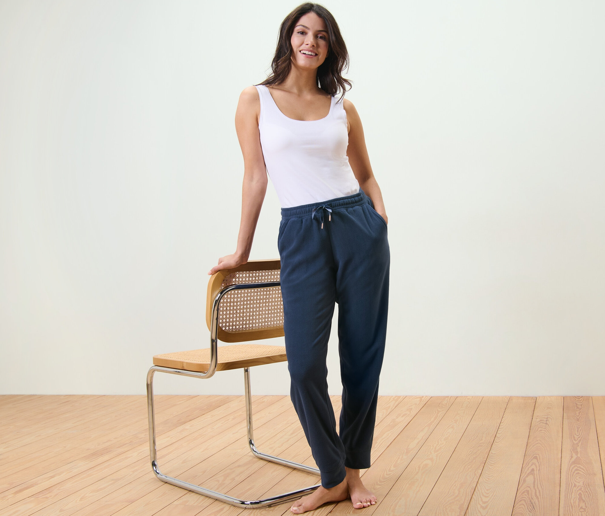Frau steht an einem Stuhl gelehnt und trägt ein Tanktop und eine Fleece-Loungehose.