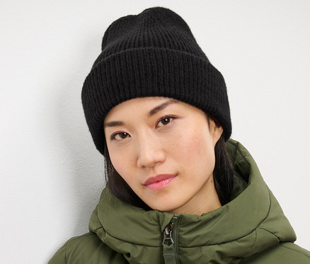 Frau trägt eine schwarze Strickmütze und eine grüne Jacke.