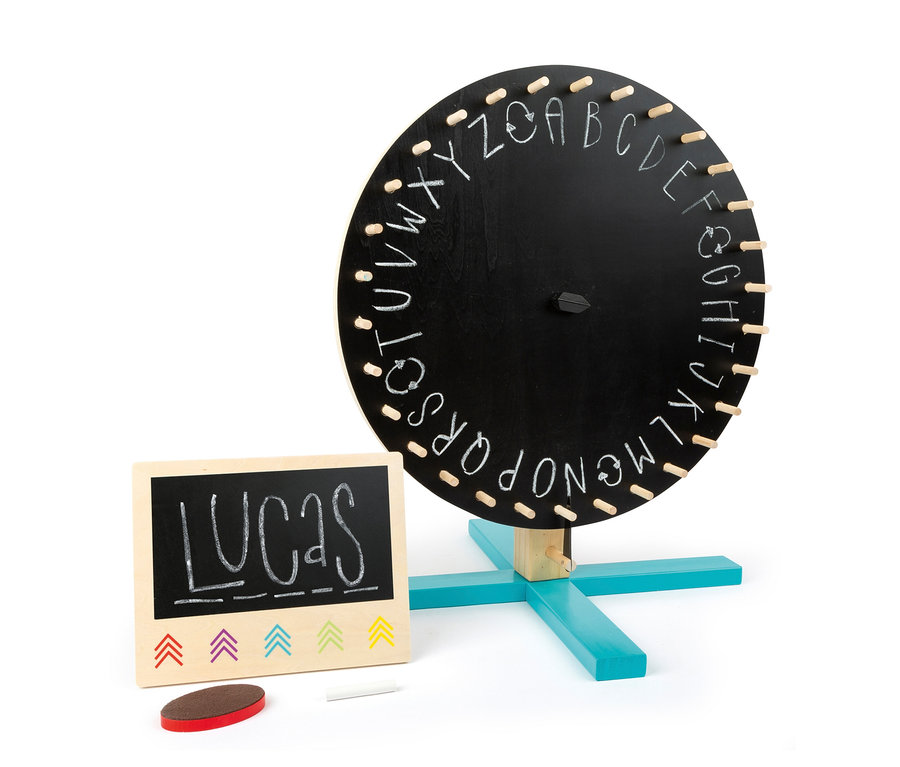 Eine schwarze Tafel mit der Aufschrift LUCAS und farbigen Pfeilen drumherum, daneben steht ein small foot Glücksrad »Active«.