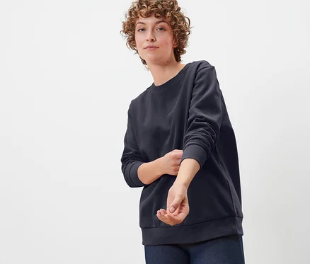 Frau mit lockigem Haar trägt ein dunkelblaues Sweatshirt.