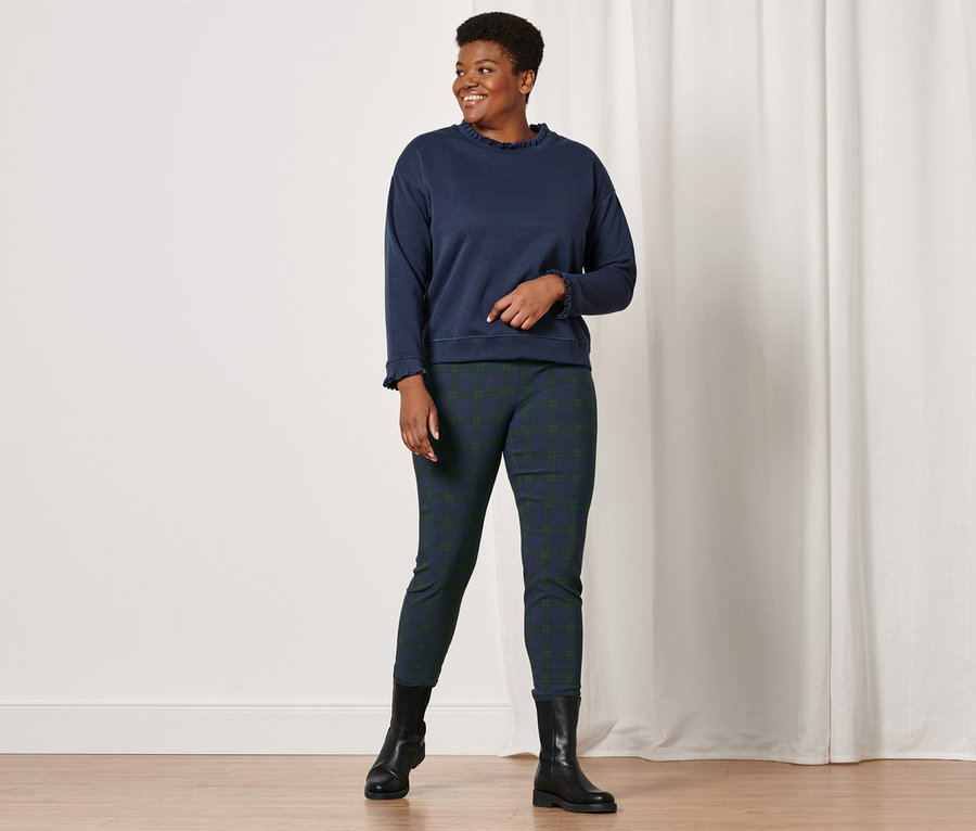 Frau posiert in Stretchhose, grün-blau kariert, und Sweatshirt mit Strickdetails.