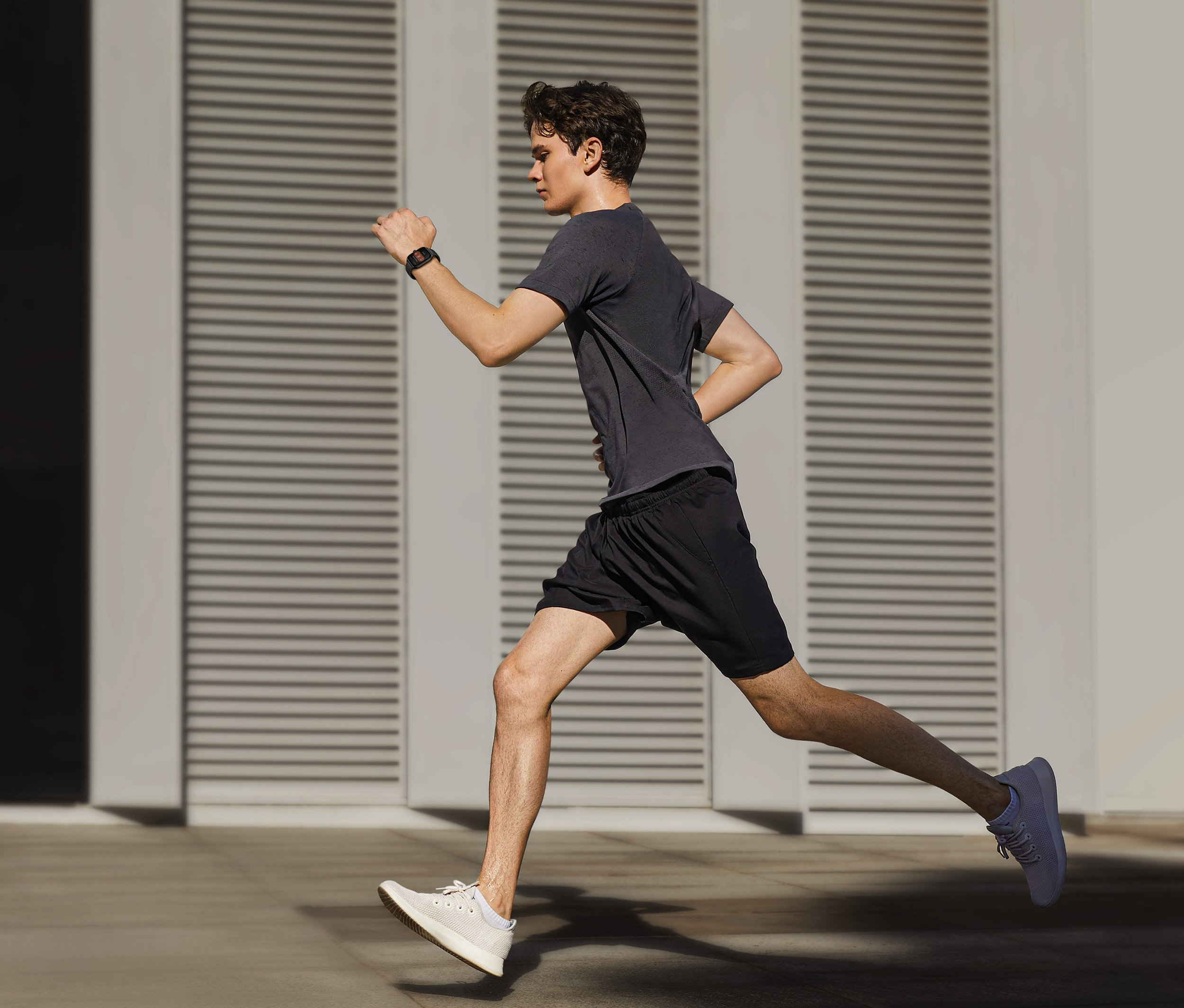 Ein junger Mann in Shorts und T-Shirt läuft draußen und trägt eine schwarze Smartwatch. Er trägt eine Amazfit GTS 4 Smartwatch, Infinity Black.