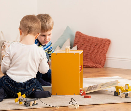 Zwei Jungen spielen mit dem Pinolino Spielwelt »Baustelle Gustav« Holzspielzeug auf einem Teppich.