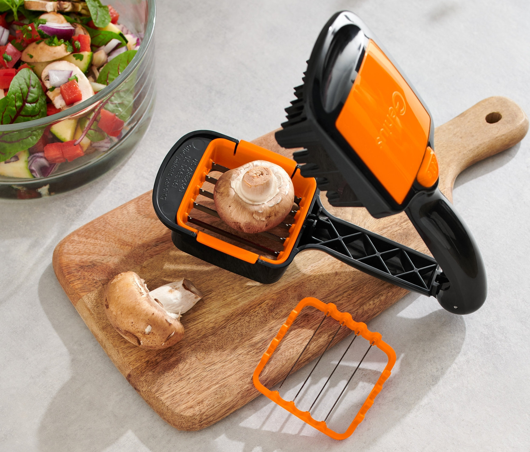 Ein Pilz im Nicer Dicer Quick XXL, 4-teilig, auf einem Schneidebrett neben Salat.