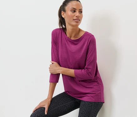 Eine Frau, die sich an eine Wand lehnt, trägt ein pinkes Funktionsshirt mit 3/4-Arm und Leggings mit Animal-Print.