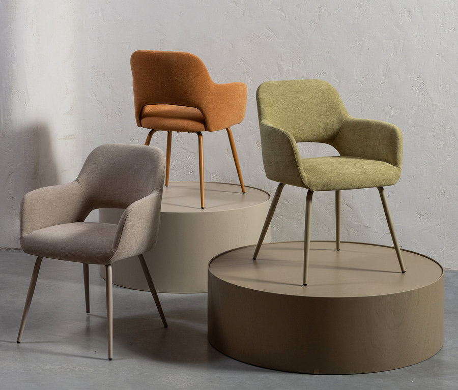 Drei Woood Jenny Stühle in Beige, Orange und Grün stehen auf Podesten.