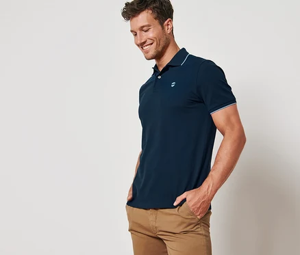 Ein lächelnder Mann posiert in einem marineblauen Piqué-Poloshirt.
