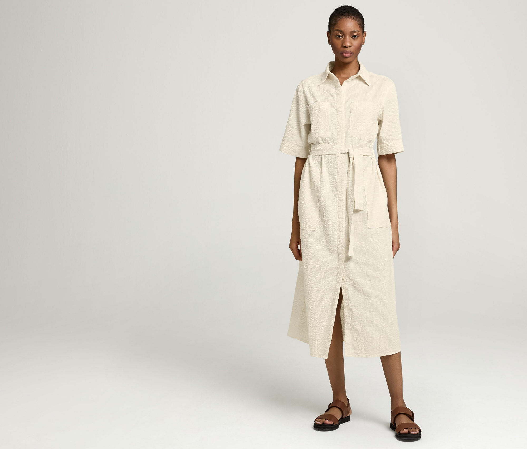 Frau trägt NAH/STUDIO Seersucker-Kleid aus ungefärbter Baumwolle und braune Sandalen.