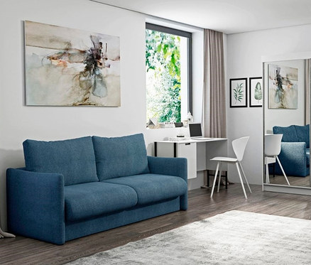 Wohnzimmer mit blauem DOMO collection Schlafsofa 2-Sitzer »Helsinki«, weißem Schreibtisch und Spiegelschrank.