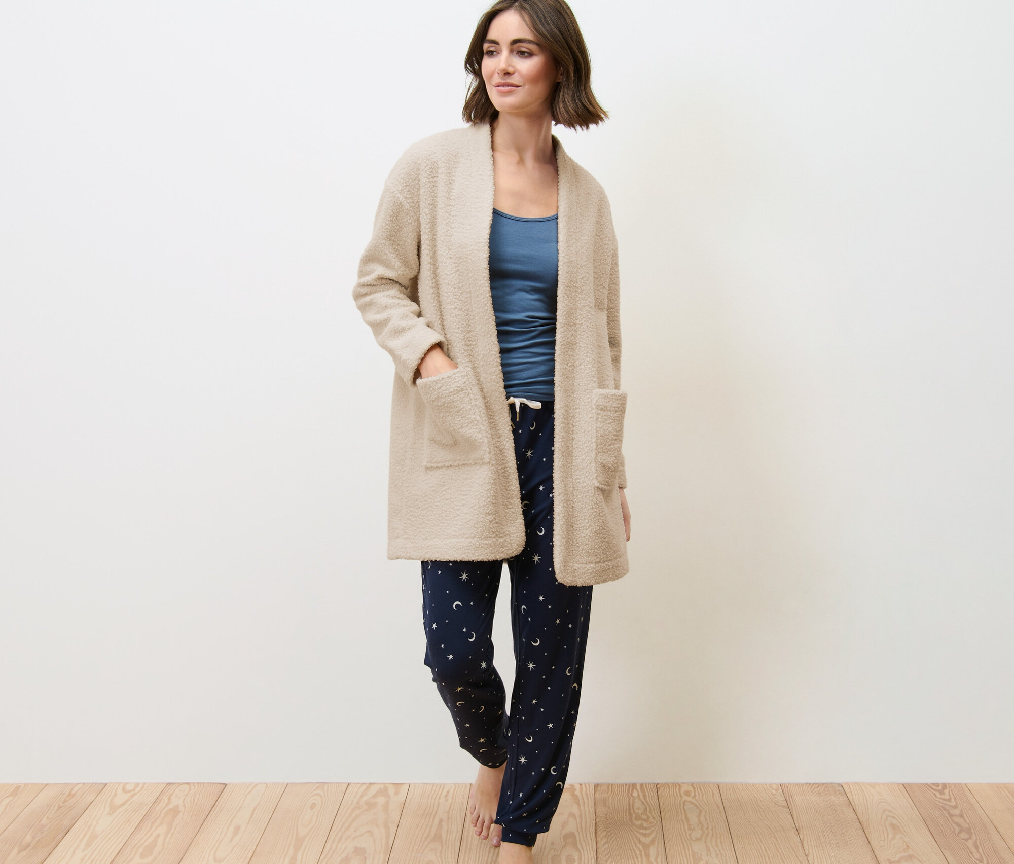 Frau trägt eine Teddyjacke, ein blaues Shirt und eine Schlafanzughose mit Sternen- und Mondmuster.