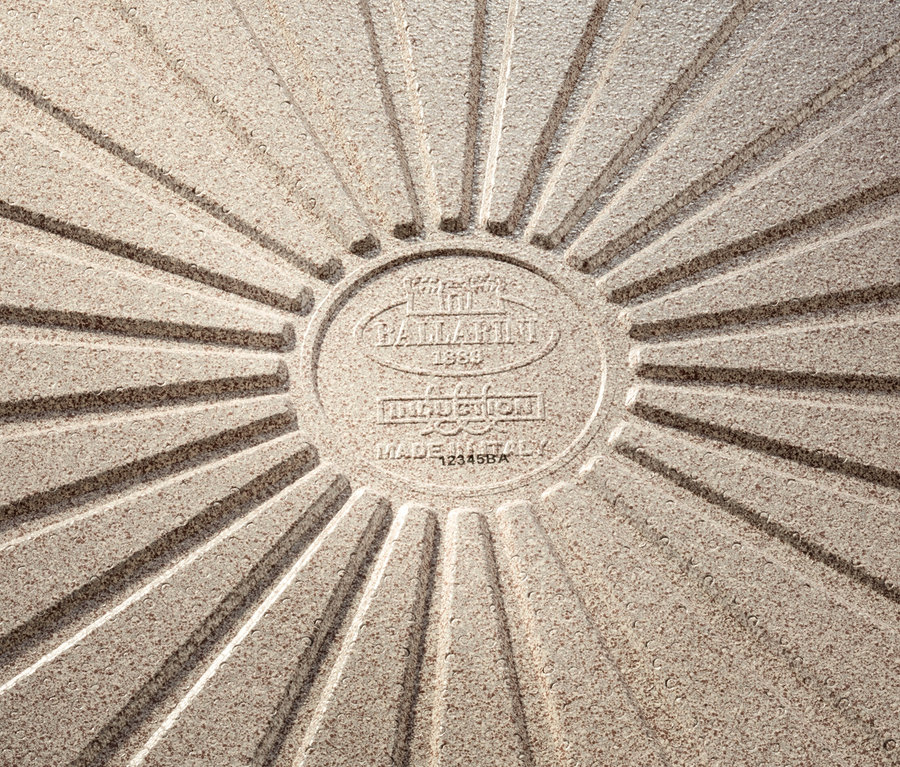 Detail der Unterseite einer Ballarini Aluminium-Bratpfanne in Sand. Das geprägte Logo und der Schriftzug "MADE IN ITALY" sind zu sehen.