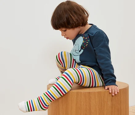 Junge sitzt auf einem Holzhocker und trägt eine geringelte Strumpfhose. 5 Paar Kinder-Strumpfhosen.