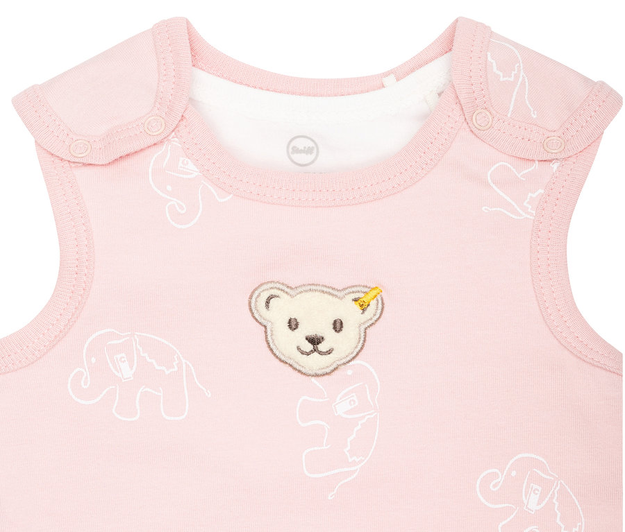 Detailaufnahme eines rosa Steiff Baby-Stramplers mit weißen Elefanten und einem Teddybär-Aufnäher.